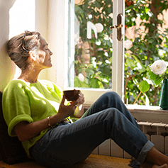 Entspannte Frau mit einer Tasse am offenen Fenster